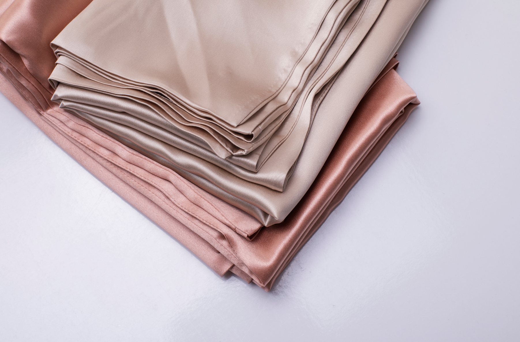 Stack of folded beige and pink satin bed sheets on white background