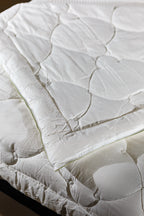 White quilted mattress topper on a bed, soft bedding accessory, close-up view