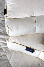 Close-up of two thick white pillows with gold piping on a bed, featuring Andazi tags