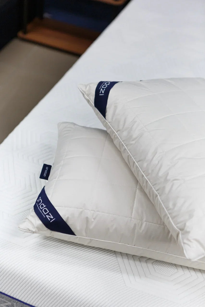Two white quilted pillows with navy trim on a white mattress in a bedroom setting