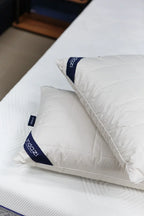 Two white quilted pillows with navy trim on a white mattress in a bedroom setting