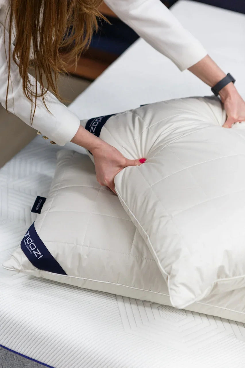 Woman pressing white quilted pillow with dark trim on a mattress, close-up