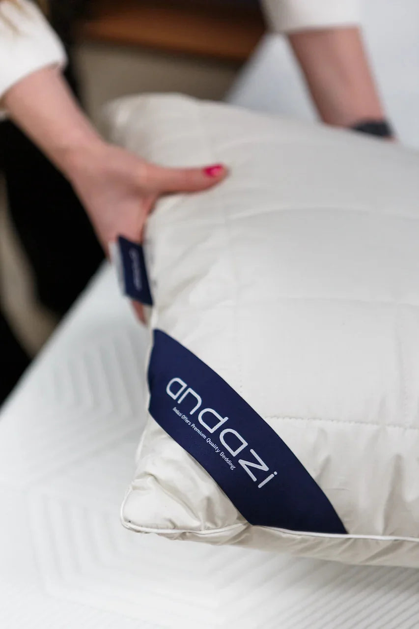 Person holding a white quilted pillow with Andazi logo on a mattress surface