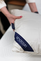 Person holding a white quilted pillow with Andazi logo on a mattress surface