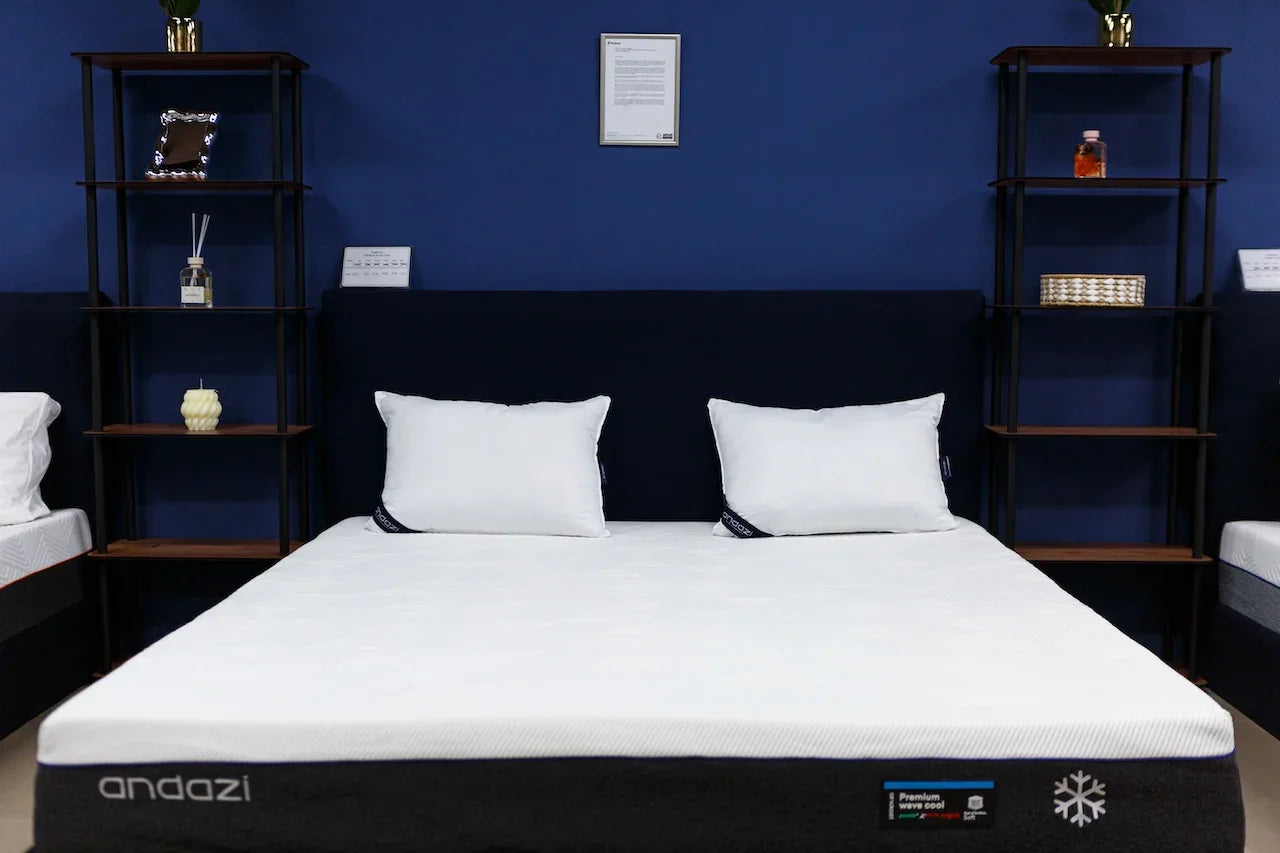 Modern bedroom with a premium mattress, white pillows, navy headboard and shelving.
