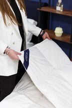 Woman in white blazer adjusting a white mattress topper on a bed in a modern bedroom