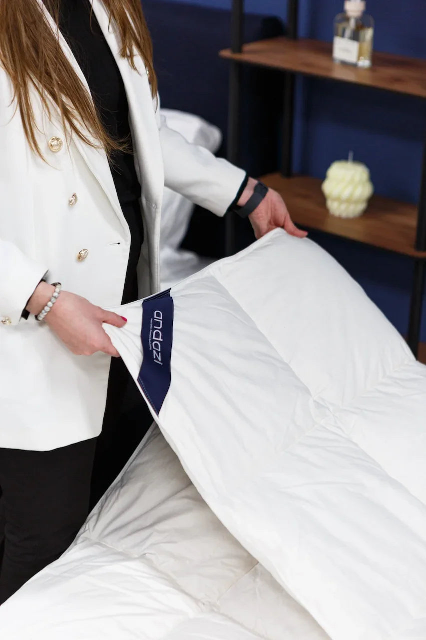 Person displaying a white quilted mattress cover with Andazi label in a bedroom setting