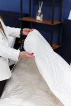 Person arranging white mattress pad on a bed in a modern bedroom setting
