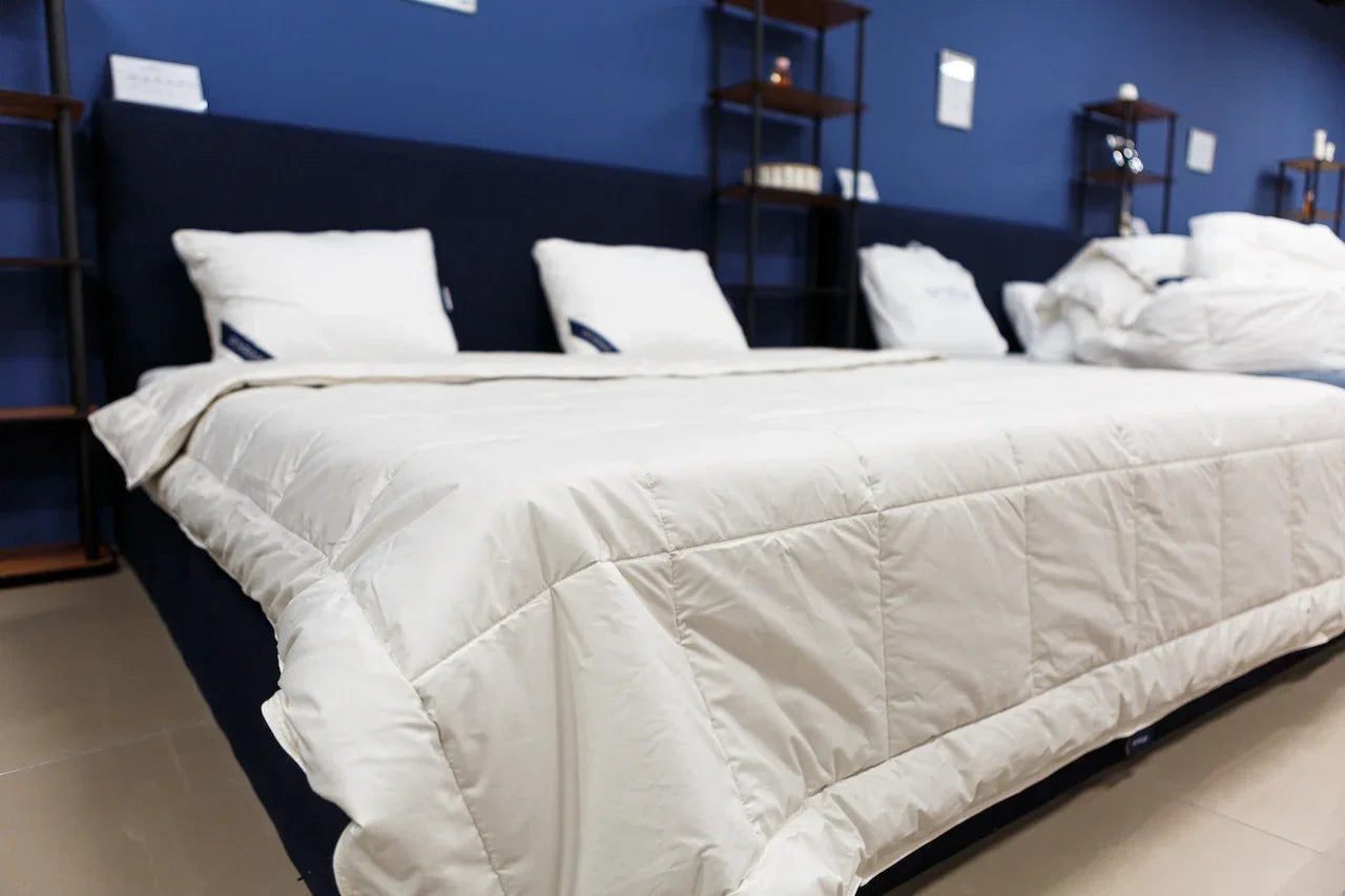 Modern bedroom with plush white mattress, soft bedding, and white pillows against a blue wall