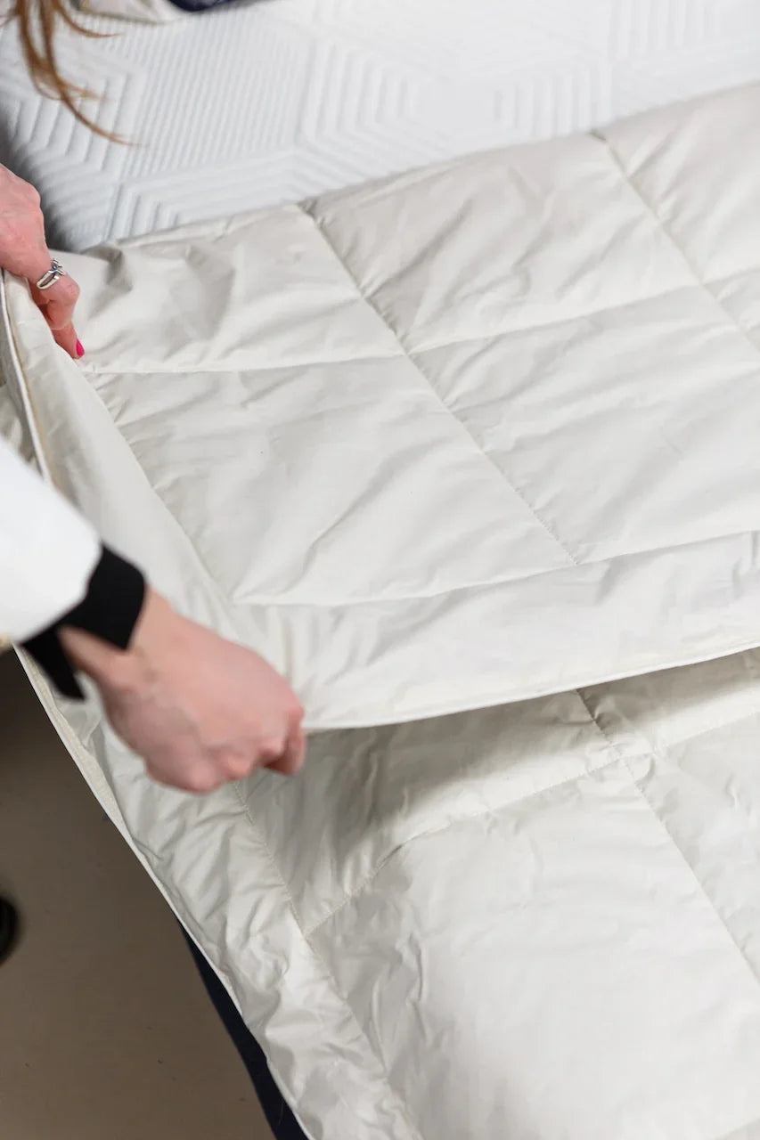 Person adjusting white quilted mattress protector on a bed