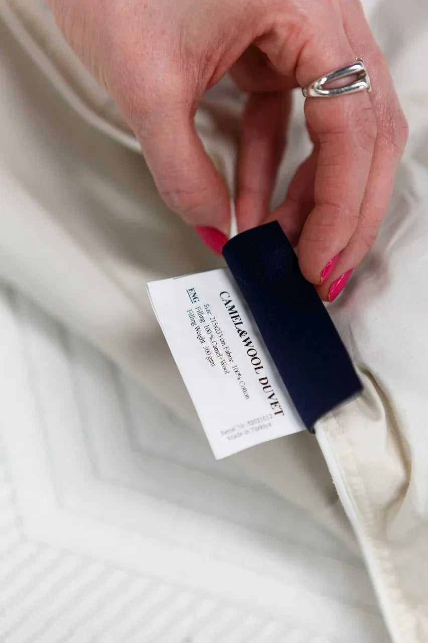 Hand holding tag on camel and wool duvet, close-up of bedding label for mattress care