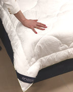 Hand pressing on a white mattress topper with quilted texture and visible andazi label