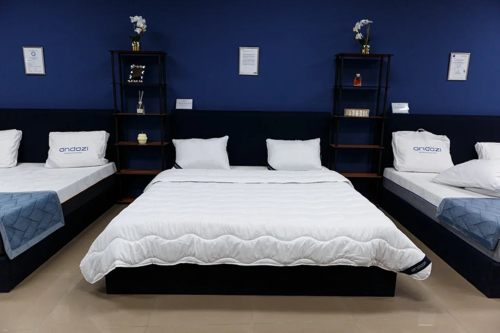 Showroom display of three white mattresses with pillows on dark bed frames against a blue wall