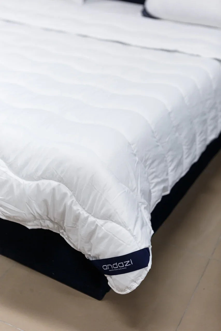 White mattress protector on bed with quilted texture and visible andazi label
