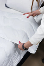 Person arranging a white, quilted mattress protector on a bed.