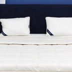 White mattress with two white pillows on a bed against a dark headboard