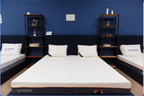 Showroom with three modern memory foam mattresses, white pillows, navy headboards, and decorative shelving.
