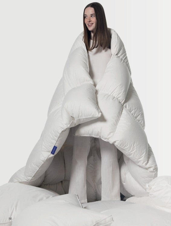 Woman wrapped in a large white comforter, cozy bedding and sleepwear setting
