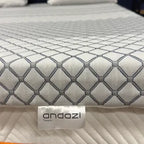Close-up of a mattress topper with geometric pattern on a bed, andazi label visible