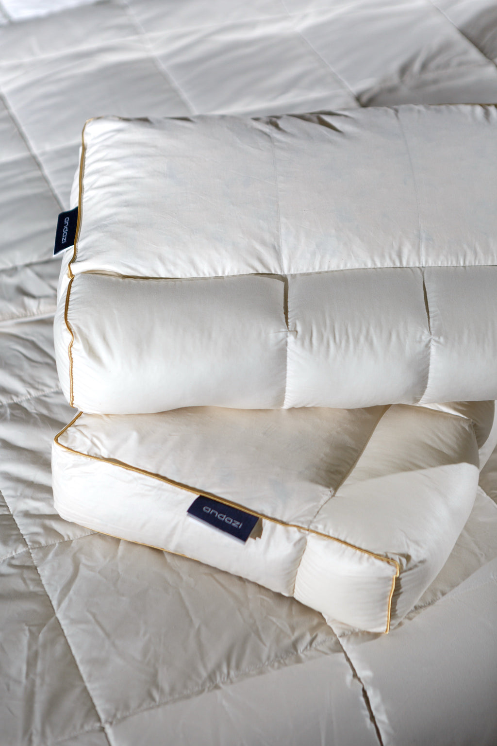 Two white ergonomic pillows with gold piping on a quilted mattress surface