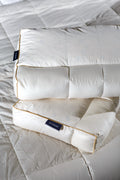 Two white ergonomic pillows with gold piping on a quilted mattress surface